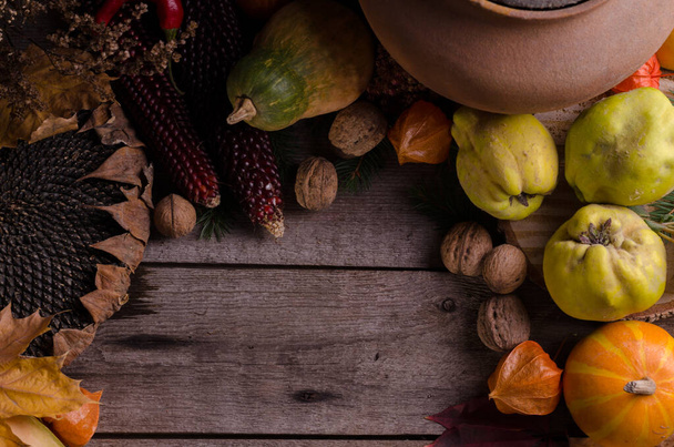 Autumnal rural frame with bright ripe pumpkins, big dry sunflower, apple quinces and nuts on an old wooden background with empty space for text. - Photo, Image