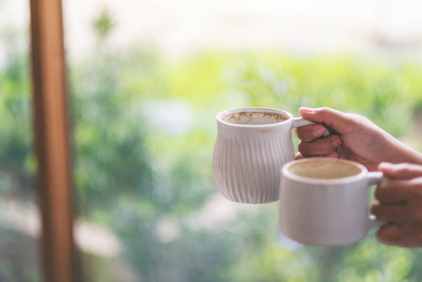 Image rapprochée de mains tenant deux tasses blanches de café chaud avec fond de nature floue
 - Photo, image