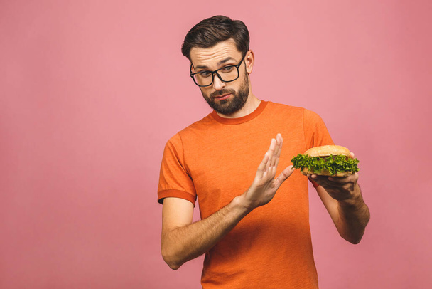 Bel giovanotto che rifiuta hamburger malsano isolato su sfondo rosa. Il concetto di dieta. Con spazio di copia per il testo
. - Foto, immagini
