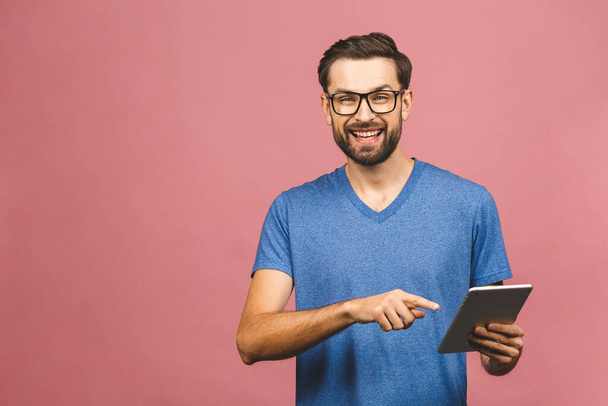 Happy young man in casual standing and using tablet over pink background - Φωτογραφία, εικόνα