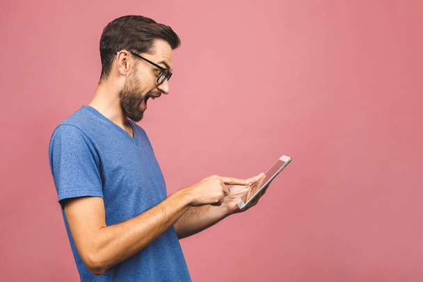 Hombre joven feliz en posición informal y el uso de la tableta aislada sobre fondo rosa
. - Foto, imagen