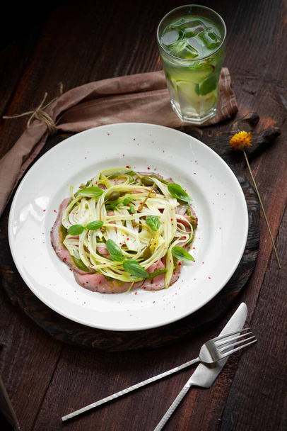 Fennel salad with beef carpaccio, Basil and pesto on a white plate. Italian gourmet snack - Photo, Image