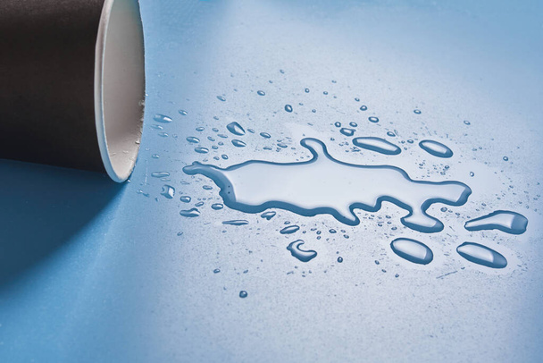 Dark Paper cup with abstract drops of spilled water on blue background. Spilled alcohol drink cup concept. - Photo, Image