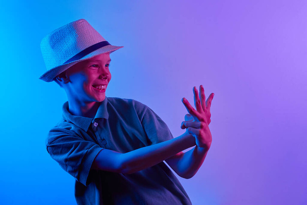 Portrait of a cool boy child stylishly posing in a straw hat on a blue and violet neon light background. - Foto, Imagen