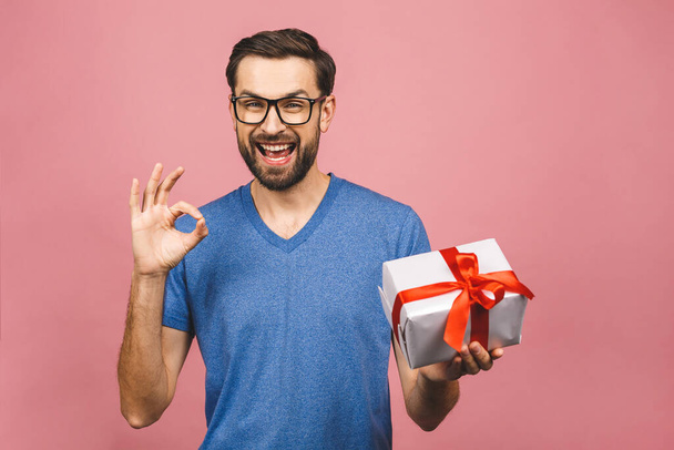 Прекрасный подарок! Очаровательная фотография привлекательного мужчины с красивой улыбкой, держащего коробку подарка на день рождения изолированы на розовом фоне. Хорошо знак
. - Фото, изображение