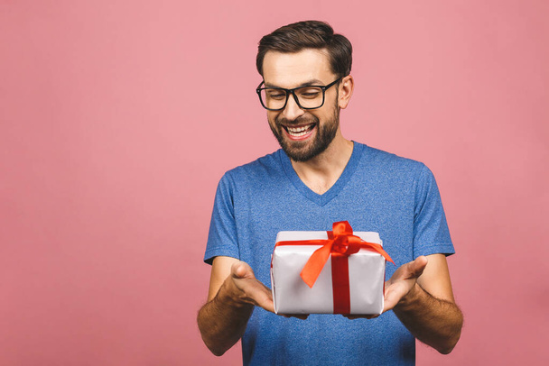 Nádherný dárek! Rozkošná fotka atraktivní muž s krásným úsměvem drží jeho narozeninové dárkové krabice izolované přes růžové pozadí. - Fotografie, Obrázek