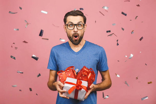 Прекрасный подарок! Симпатичное фото привлекательного мужчины с красивой улыбкой, держащего свои коробки подарков на день рождения изолированы на розовом фоне
. - Фото, изображение