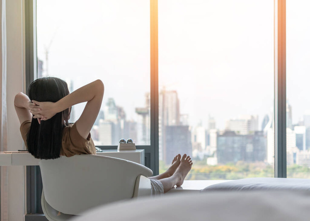 Életminőség koncepció fiatal nővel pihentető és pihentető kényelem üzleti hotel vendégszoba vagy luxus otthon nappali felé néző gyönyörű kilátás a városra - Fotó, kép