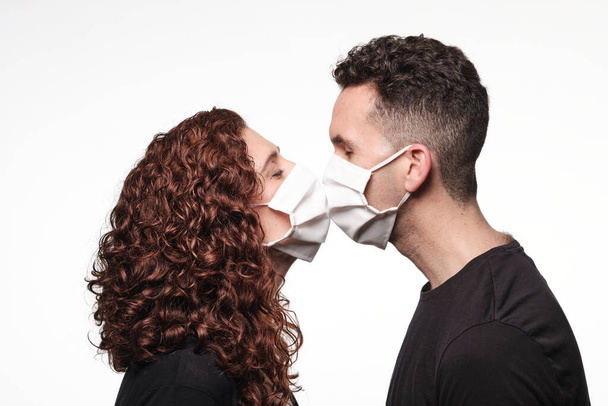 Νεαρός άντρας και γυναίκα δίνουν ένα φιλί φορώντας προστατευτική μάσκα για τον κορωναϊό - Φωτογραφία, εικόνα