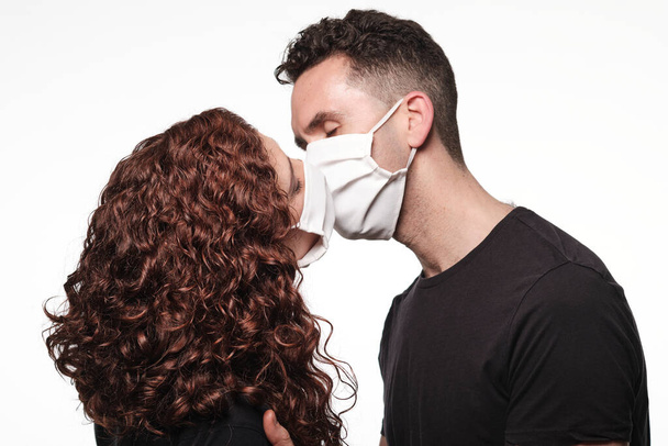 Young man and woman giving a kiss wearing a protective mask for coronavirus - Fotó, kép