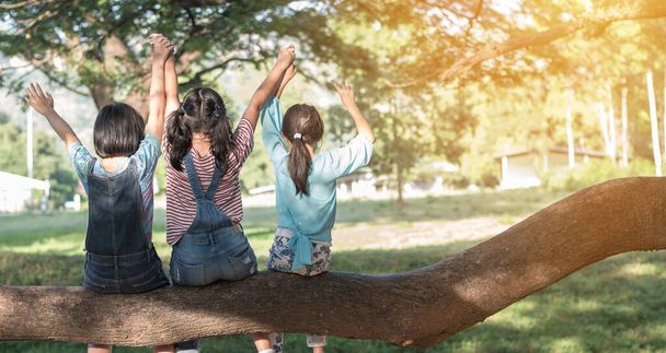 公園の幸せな女の子の子供たちとの子供の友情の概念は、学校の時間帯に友人と一緒に楽しい思い出と学生生活の瞬間を楽しんで一緒に遊んで木陰に座って楽しんでいます - 写真・画像