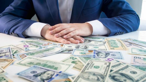 Mannelijke zakenman die handjes vasthoudt op een bureau bedekt met geld. Begrip financiële investering, economische groei en spaargeld van banken - Foto, afbeelding