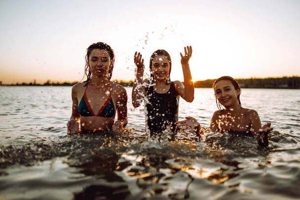 Young girls squirting and having fun in the sea at sunset. Beach holiday and summer vacation concept. - Fotografie, Obrázek