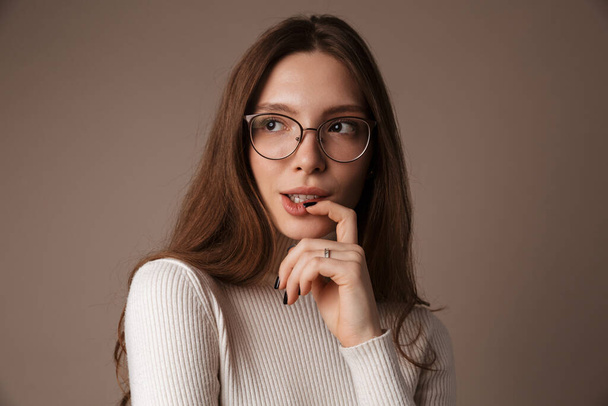 Photo of thinking beautiful woman in eyeglasses posing and looking aside isolated over grey wall - Foto, immagini