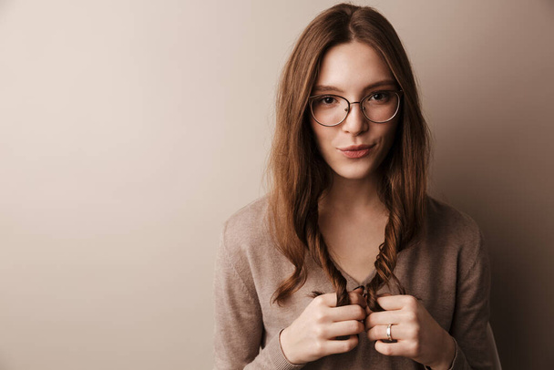 Photo of young beautiful woman in eyeglasses posing and looking at camera isolated over grey wall - Zdjęcie, obraz