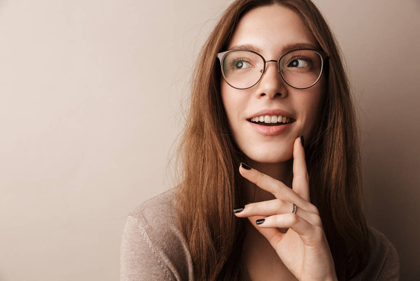 Photo of young happy woman in eyeglasses smiling and looking aside isolated over grey wall - Photo, image