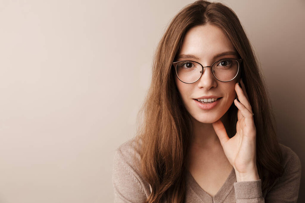 Photo of young happy woman in eyeglasses smiling and looking at camera isolated over grey wall - Fotografie, Obrázek