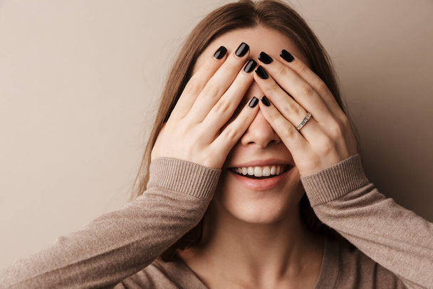 Фотографія молодої щасливої жінки, яка посміхається і закриває очі ізольовано над сірою стіною
 - Фото, зображення