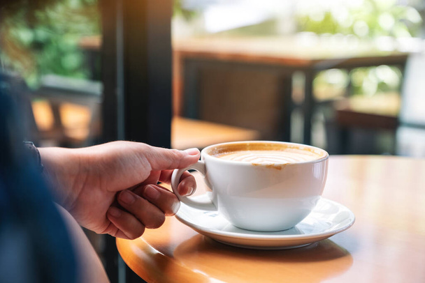 Close-up afbeelding van een hand met een kopje hete koffie op tafel - Foto, afbeelding