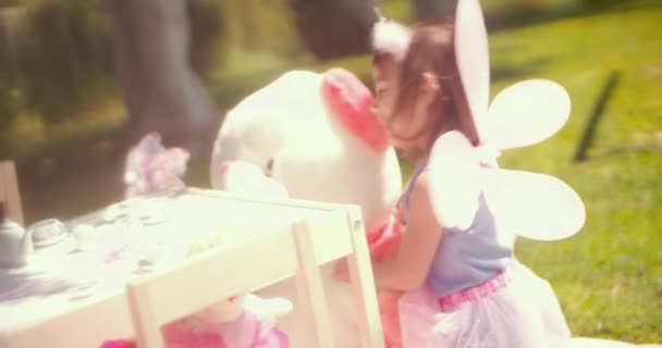 Little girl in fairy costume hugging teddy bear in garden - Кадры, видео