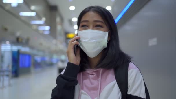 Aziatische jonge vrouw dragen beschermende masker praten op de telefoon luchthaven grote hal, luchthaven terminal, veilige reis van virus covid-19 pandemie, nieuwe normale sociale afstand concept, slow motion - Video