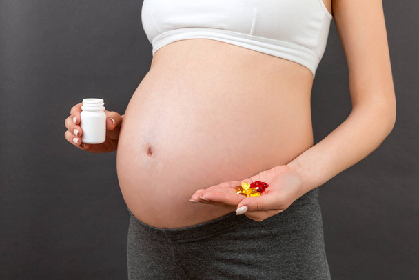 Close-up van een fles en hoop pillen in handen van zwangere vrouw op kleurrijke achtergrond met kopieerruimte. Gezond zwangerschapsconcept. - Foto, afbeelding
