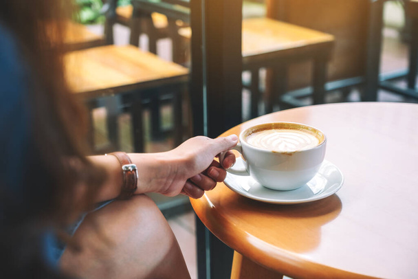 Imagen de cerca de una mujer sosteniendo una taza de café caliente en la mesa
 - Foto, imagen
