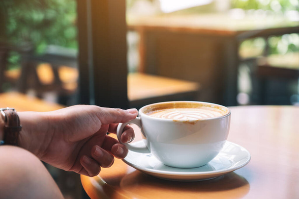 Closeup image of a hand holding a cup of hot coffee on table - Photo, Image