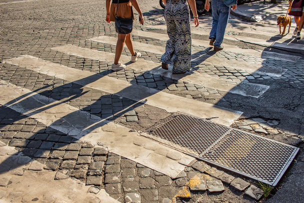 Rome Italy. Some people cross a typical Roman cobblestone street, passing on the pedestrian crossings. Framing on the legs and feet. - Fotoğraf, Görsel