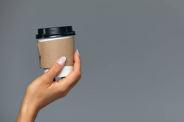 Χέρι κοριτσιού που κρατάει ένα χάρτινο φλιτζάνι καφέ, γκρι φόντο Καλημέρα, έννοια. Κενό μέρος για μια επιγραφή. - Φωτογραφία, εικόνα