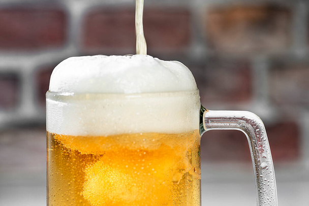 Закрыть подачу освежающего пива кружку с пеной на белом баре и красного кирпича стены фона
 - Фото, изображение