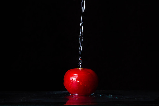 Pomodoro rosso su fondo nero. l'acqua versa su un pomodoro dall'alto
 - Foto, immagini
