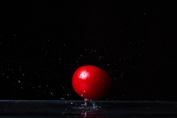  Pomodoro rosso su fondo nero. Il pomodoro cade in acqua
. - Foto, immagini