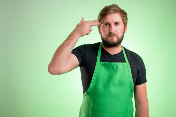 Сотрудник супермаркета в зеленом фартуке и черной футболке с вывеской на зеленом фоне
 - Фото, изображение