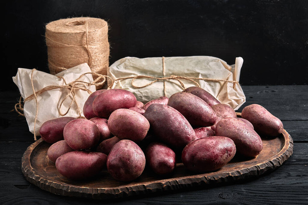 Κόκκινες πατάτες σε σκούρο ξύλινο φόντο. Σχέδιο παράδοσης τροφίμων, φιλική προς το περιβάλλον συσκευασία. Αντιγραφή χώρου, κοντινό - Φωτογραφία, εικόνα