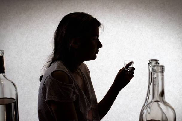 Vrouw houdt een glas met sterke alcohol vast. Vrouwelijk alcoholisme, alcoholverslaving, delirium tremens. Silhouet foto. - Foto, afbeelding