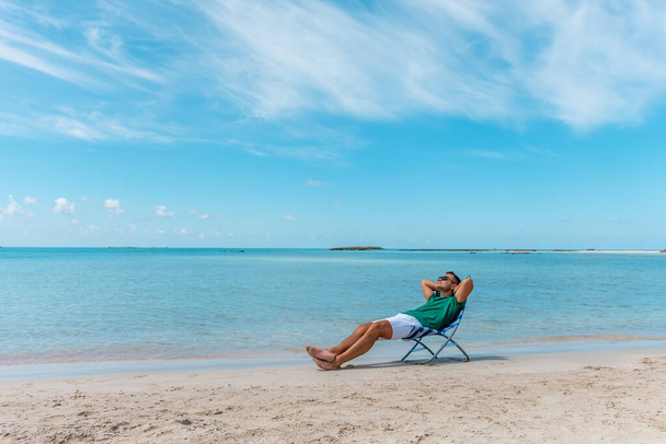 Man is sitting in chair on a tropical beach. Summer vacation concept. - Photo, image