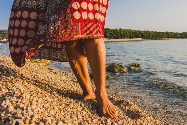 Kobieta z gołymi stopami stojąca na mokrych kamieniach wybrzeża morskiego, zbliżenie. - Zdjęcie, obraz