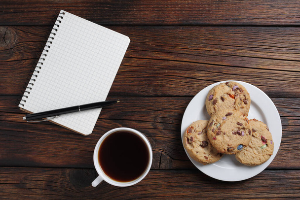 Cup of coffee, cookies and notebook with pen on wooden background, top view - Photo, Image