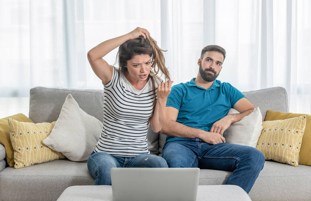 Young guy gets bored while his girlfriend shows her friend online over the laptop how her hairdresser ruined her hair - Φωτογραφία, εικόνα