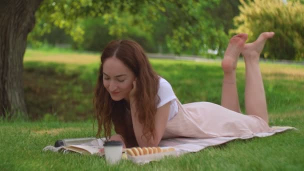 Jonge vrouw ligt en leest een boek in het park - Video