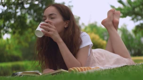 Young pretty woman drinking coffee on a grass in a summer park. - Materiaali, video