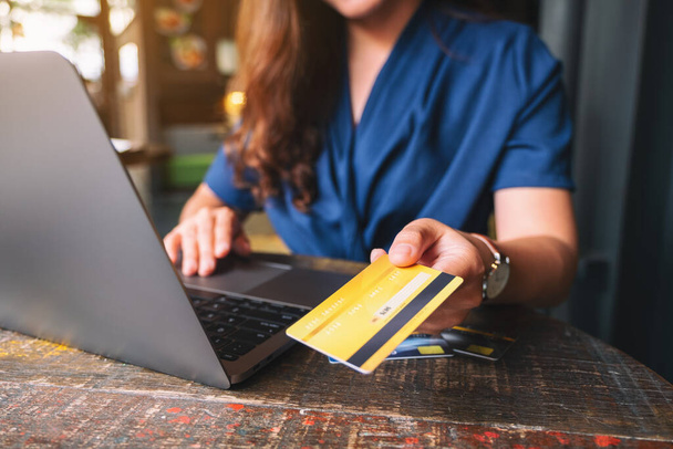 Een vrouw die een creditcard vasthoudt en aan iemand geeft terwijl ze een laptop gebruikt - Foto, afbeelding