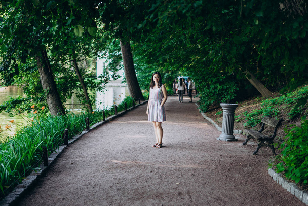 Sofia Park, Uman. Meisje in een zomerbord in de steeg van het park. Lachend brunette meisje in een stenen steegje bij het meer. Wandeling in het park, een groot mooi meer - Foto, afbeelding