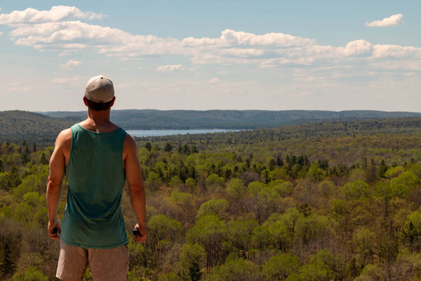Вид сзади на человека, сидящего на скале над пейзажем - Фото, изображение