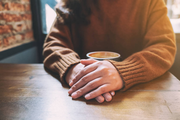 Closeup image of a woman sitting with a cup of hot coffee on wooden table - Photo, Image