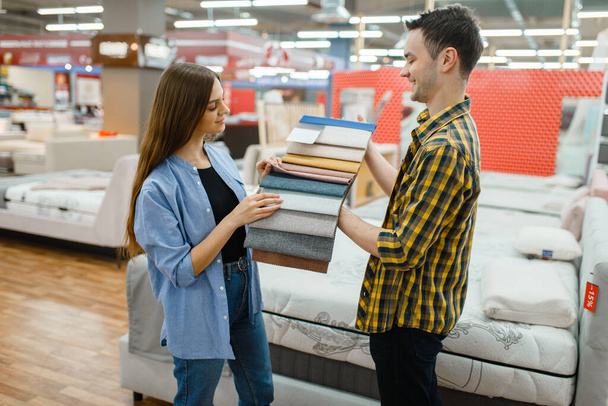 Young love couple choosing texture of mattress in furniture store showroom. Man and woman looking samples for bedroom in shop, husband and wife buys goods for modern home interior - Foto, Bild