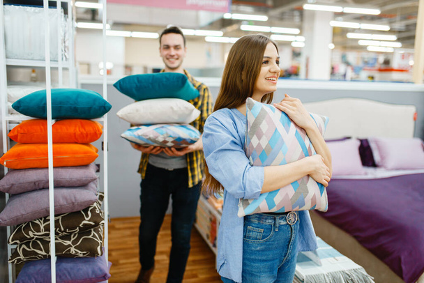 Young love couple holds pillows in furniture store. Man and woman looking samples for bedroom in shop, husband and wife buys goods for modern home interior - Photo, Image