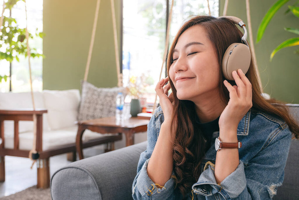 Egy gyönyörű ázsiai nő élvezi hallgatni a zenét fejhallgatóval érzés boldog és nyugodt kávézóban - Fotó, kép