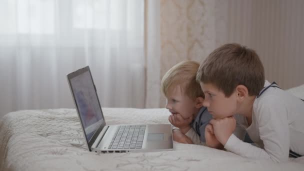 söpö pieni lapsi poika käyttää opetussovellus tietokoneella istuu sohvalla pienempien hymyilevä veli nauttia hauskaa - Materiaali, video